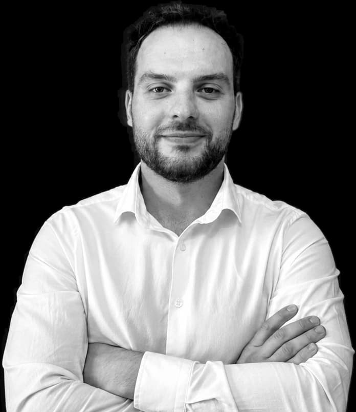 Fatjon (Tony) Kalemaj, COO and Head of Applied AI at By The People Technologies, in black and white, in an open-collared white shirt, arms folded.