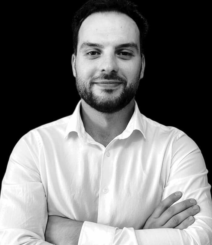 Fatjon (Tony) Kalemaj, COO and Head of Applied AI at By The People Technologies, in black and white, in an open-collared white shirt, arms folded.